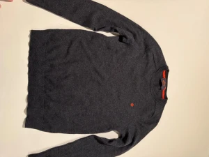 Mörkgrå merinoulltröja från Morris - Snygg mörkgrå stickad tröja från Morris i 100% merinoull. Klassisk rund hals med orange detaljer och liten broderad logga på bröstet. Perfekt för dig som gillar stilrena och bekväma plagg med premiumkänsla. Passar strl S-XS