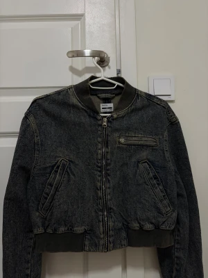  jeans bomberjacka från Bershka - Säljer en mörkgrå bomberjacka i jeansmaterial från Bershka. Jackan har ribbade muddar, dragkedja framtill och en cool bröstficka med dragkedja. Croppad passform och klassisk bomberkrage ger en snygg streetstil. Perfekt för dig som gillar denim och vill sticka ut.Helt ny har aldrig använt den 