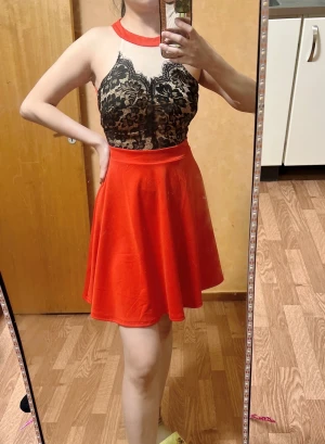 Röd klänning med spetsdetaljer ärmlös  - Säljer en snygg röd klänning med svart blommig spets upptill och hög hals. Klänningen har en vid kjol och är ärmlös, perfekt för festliga tillfällen. Stängs med dragkedja i ryggen och har en elegant design.