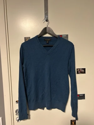Blå v-ringad tröja Banana Republic - Säljer en stilren blå v-ringad tröja från Banana Republic i storlek S. Tröjan är långärmad och gjord i en mjuk blandning av ull och kashmir, vilket gör den både skön och lätt att bära. Perfekt för dig som gillar klassisk och enkel stil.