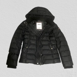 Svart dunjacka Hilfiger Denim XS - Svart dunjacka från Hilfiger Denim i storlek XS. Jackan har huva, quiltad design och dragkedja framtill. Klassisk logga på ärmen och snygga detaljer. Perfekt för kalla dagar när du vill hålla stilen.