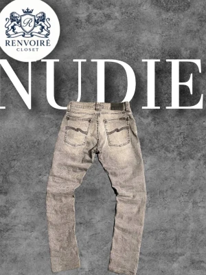 Grå jeans från Nudie - Säljer ett par grå jeans från Nudie med klassisk femficksdesign och snygga detaljer på bakfickorna. Jeansen har en slim passform och är tillverkade i slitstarkt denimmaterial. Perfekt för dig som gillar en avslappnad och stilren look. Waist 27