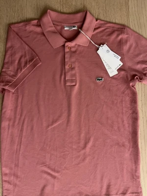 Lacoste piké rosa - Helt ny rosa Lacoste piké med lapp kvar, endast testad på annars inte använd, storlek M, nypris ca 900kr. Priset är inte hugget i sten. Tveka inte att höra av dig vid minsta fundering!