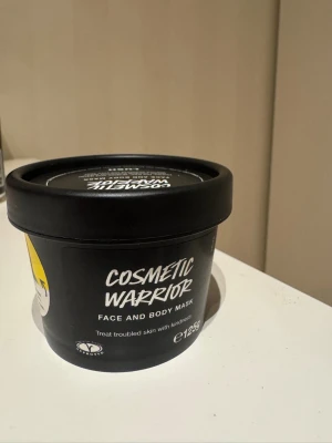 Cosmetic Warrior ansiktsmask från Lush - Cosmetic Warrior är en ansikts- och kroppsmask från Lush i en svart rund plastburk på 125g. Masken innehåller honung, tea tree, vindruvor och vitlök som lugnar och motverkar rodnad. Formulan är krämig och passar känslig hud. Innehåller ekologisk avokadoolja.