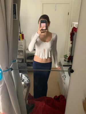 Vit croppad blus med spetskant💕 - Säljer en vit croppad blus med lång ärm och söt spetskant runt halsringningen. Toppen har en liten rosett framtill och volang nedtill som ger en feminin touch. Materialet känns mjukt och stretchigt, perfekt för dig som gillar en slim passform.🩷