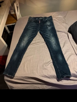 Dsquared2 blå jeans med slitningar - Snygga blå jeans från Dsquared2 med coola slitningar och tvättade detaljer. Modellen har en smal passform och klassisk femficksdesign. Perfekta för dig som gillar streetstyle och vill ha ett par jeans med attityd. Materialet är jeans och färgen är mörkblå.