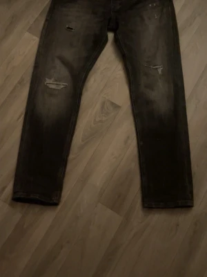 Svarta jeans från Jack & Jones - Säljer ett par svarta jeans från Jack & Jones med slitna detaljer och raka ben. Jeansen har klassisk femficksdesign och är tillverkade i ett stretchigt jeanstyg som ger en skön passform. Perfekta för dig som gillar en avslappnad och trendig look. Fåtal använd så det är ny