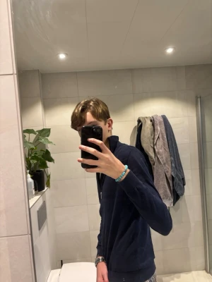 Marinblå kofta från Selected Homme - Säljer en marinblå kofta från Selected Homme med dragkedja hela vägen och ståkrage. Tröjan är långärmad och gjord i mjuk bomull, perfekt för lager-på-lager. Enkel och stilren design som funkar till det mesta.