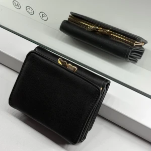 Svart plånbok  - Snygg svart plånbok i skinn med guldfärgade detaljer och hjärtformad lås. Plånboken har flera kortfack, fönster för ID och ett myntfack med metallram. Perfekt storlek för att ha med sig överallt och håller dina grejer organiserade.