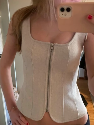 Ljusgrå korsett-topp från Zara - Supersnygg ljusgrå korsett-topp från Zara med dragkedja framtill. Toppen har breda axelband, markerade sömmar och en figurnära passform. ❣️