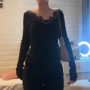 Svart långärmad topp med spets - Säljer en svart långärmad topp med v-ringning och fina spetsdetaljer runt halsen. Toppen har en slim passform och är perfekt för dig som gillar en enkel men ändå elegant stil.