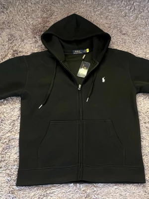 Polo Ralph lauren tröja med dragkedja - Hej!  Jag säljer en Ralph lauren kofta. Den är helt ny och har bara testat den en gång, riktig sjuk kvalité. Jag säljer den eftersom jag fick den i present och den var lite för stor. Den passar både M och L men hade nog sutit bättre på L.        Pris kan diskuteras!