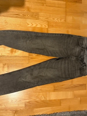 Grå Jack&Jones jeans - Säljer ett par grå Jack&Jones jeans med klassisk femficksdesign och raka ben. Jeansen har en mörkgrå tvätt och Jack&Jones logga på bakfickan samt svart patch i midjan. Perfekt för dig som gillar en enkel och clean look.