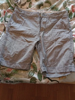 Shorts från Race Marine - Säl soprena randiga shorts från Race Marine i vitt och marinblått. Klassisk passform med fickor fram och bak, bälteshällor och dragkedja. Perfekta för sommardagar och chill häng. Materialet känns som bomull och är riktigt skönt mot huden. Kan behövas strycka. Pris kan sänkas vid en villig affär