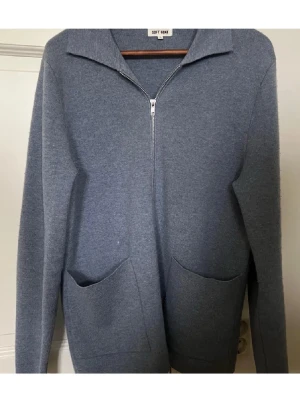 Blå zip-kofta från Soft Goat - Snygg blå kofta från Soft Goat i storlek M. Koftan har en rak passform, långa ärmar, två stora fickor framtill och dragkedja hela vägen upp till kragen. Materialet är mjukt och stickat, perfekt för kyliga dagar.
