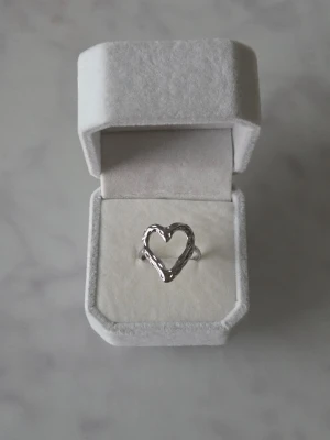 Ring med hjärtformad  - Säljer en snygg ring med ett öppet hjärta som motiv. Ringen har en lite vågig och organisk form som ger den en cool och unik vibe. Perfekt att bära som statement piece eller att kombinera med andra smycken.