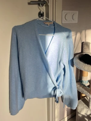 Ljusblå omlottkofta Pernilla Wahlgren XS - Säljer en supermjuk ljusblå omlottkofta från Pernilla Wahlgren i storlek XS. Koftan har långa ärmar, v-ringad hals och knyt i sidan för en snygg passform. Perfekt för lager-på-lager och chill dagar. Materialet är stickat och är riktigt skönt mot huden. Har bara använts en gång. Passar både till chill och fint 🥰❤️❤️