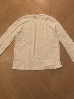 Vit långärmad topp från 157 - En enkel och stilren vit långärmad topp från 157, tillverkad i 100% bomull. Modellen har rund hals och en rak passform som är lätt att matcha med olika outfits. Perfekt för dig som gillar basic och cleana plagg.