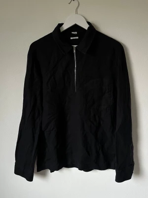 Svart Arket långärmad skjorta med dragkedja - Svart skjorta i regular fit med lång ärm och dragkedja framtill. Skjortan har klassisk krage, bröstficka och är tillverkad i en blandning av lyocell och linne. Perfekt för dig som gillar stilrena och enkla plagg med lite edge. 5M11