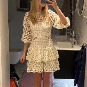 Vit spetsklänning med volanger - Superfin vit kortklänning med spets och volanger. Klänningen har trekvartsärmar, högt halslinje och snygga detaljer med genombruten spets. Endast använd 1 gång! Storlek xs men passar mig som brukar ha s