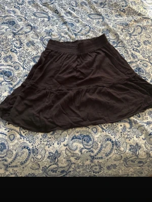 Svart volangkjol från C, storlek S - Säljer en svart kortkjol från C i storlek S. Kjolen har en mjuk resår i midjan och volangdetalj som ger en snygg och avslappnad look. Materialet känns lätt och skönt mot huden, perfekt för dig som gillar enkel stil med lite extra flärd.