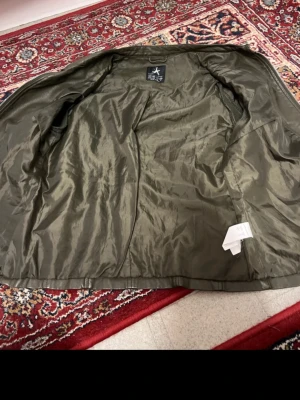 Olivgrön skinnjacka från Atmosphere - Snygg olivgrön skinnjacka från Atmosphere i storlek 36. Jackan har coola quiltade detaljer på axlar och sidor, två dragkedjeförsedda fickor framtill och en rak passform. Materialet är syntetiskt skinn med ett lent foder. Perfekt för dig som gillar en edgy stil.