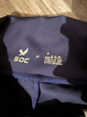 Mörkblå träningsbyxor från SOC - Snygga mörkblå träningsbyxor från SOC med bred midja och raka ben. Materialet är mjukt och stretchigt polyester som andas och håller dig bekväm. Perfekta för gymmet eller andra sportaktiviteter. Diskret logga på höften och minimalistisk design. Storlek S.