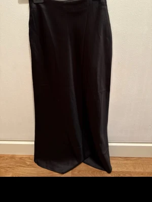 Svart långkjol från NA-KD i satin - Säljer en svart långkjol från NA-KD i storlek 32. Kjolen har en stilren och slät design med lätt glansigt satintyg som ger en snygg och modern look. Perfekt för dig som gillar minimalistisk stil och vill ha något som känns både trendigt och bekvämt.