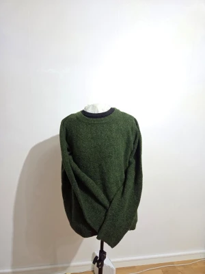 Grön stickad tröja från H&M - Mörkgrön stickad tröja från H&M i storlek M. Tröjan har rund halsringning och långa ärmar, med en mjuk och lite grov stickad struktur. Perfekt för dig som gillar enkel och chill stil med lite extra värme.