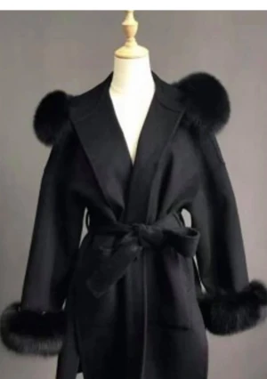 Svart kappa med pälsdetaljer och bälte - Snygg svart kappa med fluffiga pälsdetaljer på axlar och ärmslut. Jackan har ett brett bälte i midjan som knyts och ger en cool siluett. Perfekt för dig som vill sticka ut med en elegant och trendig look.