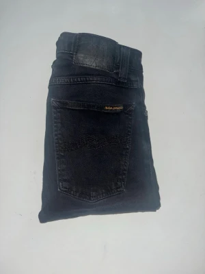 Nudie Jeans - Säljer ett par svarta skinny jeans från Nudie Jeans. Jeansen har klassisk femficksdesign, smal passform och är tillverkade i mjukt jeansmaterial. Midja 29cm, längd 92cm. JAG SKICKAR EJ FLER BILDER NÄR JAG BÄR JEANSEN! för storleksguide hänvisar jag till måtten och för bättre inblick i passformen rekommenderar jag att googla på modellnamnet. kolla måtten noggrant :) s5,1