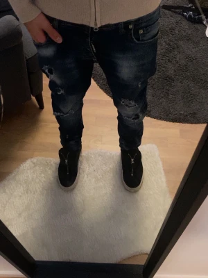 Mörkblå slitna jeans med skinny fit - Säljer ett par mörkblå jeans med skinny passform och snygga slitningar på benen. Jeansen har klassisk femficksdesign och är gjorda i jeansmaterial. Perfekta för dig som gillar en tuff och trendig stil.