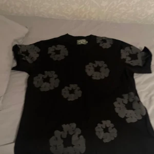 Svart t-shirt med blommigt mönster - Svart t-shirt med coola blommiga tryck över hela framsidan. Klassisk rund hals och korta ärmar. Materialet känns mjukt och skönt, troligtvis bomull. Perfekt för dig som vill sticka ut med ett unikt mönster.