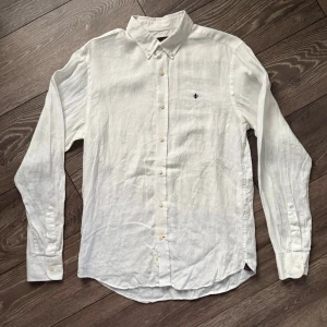 Vit linneskjorta från Morris - Fräsch vit skjorta från Morris i ren linne, perfekt för varma dagar. Klassisk button-down krage, långärmad och med snygga knappar framtill. Broderad logga på bröstet ger en stilren touch. Skön och luftig passform, passar dig som gillar enkel och clean stil. Lite missfärgad i armhålorna