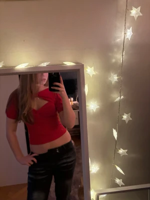 Röd croppad omlottopp - Säljer en röd croppad topp med omlottdetalj och snygg twistad v-ringning. Toppen har korta ärmar och ett öppet parti vid bröstet som ger en cool look. Materialet känns mjukt och stretchigt, perfekt för att styla med jeans eller kjol.