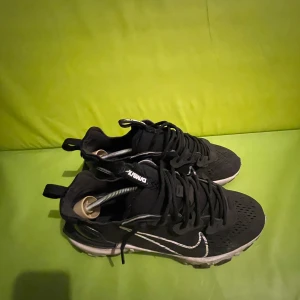 Svart/vit Nike React Vision - Svarta Nike sneakers med vit swoosh och snörning. Ovandelen är i ventilerande syntetmaterial och sulan har en unik design med synliga dämpningskuddar. Den har ett litet hål på båda skorna men inget som syns så mycket. Perfekt för dig som gillar sportig stil och vill ha bekväma skor med cool look. Inga returer.