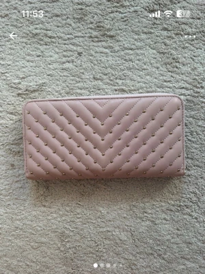 Rosa quiltad plånbok med dragkedja - Säljer en snygg rosa plånbok med quiltad design och små guldfärgade nitar. Plånboken har dragkedja runtom och flera fack för kort, sedlar och mynt. Perfekt storlek för att ha med sig överallt och håller ordning på allt viktigt. 20x10 cm