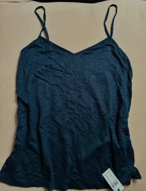 Mörkblå linnetopp från Intimissimi - Säljer en stilren mörkblå linnetopp från Intimissimi, designad i Italien. Toppen har smala justerbara axelband med metallringar och en v-ringad hals. Materialet är mjukt linne som känns svalt och skönt mot huden.  Lös modell. Ny med taggar. Nypris 400 kr