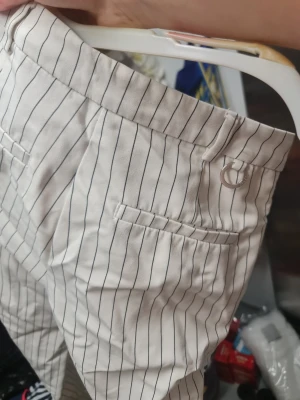 Randiga vita byxor från STOCKH LM - Snygga vita byxor med svarta vertikala ränder från STOCKH LM, storlek 34. Byxorna har croppad längd, fickor fram och bak samt hällor för bälte. Tillverkade i mjukt bomullsmaterial och har en klassisk, slim passform som ger en fräsch look.