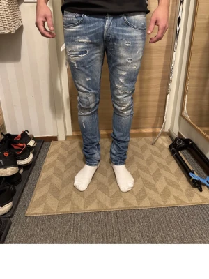 Blå skinny jeans med slitningar - Säljer ett par ljusblå skinny jeans med slitna detaljer och färgstänk för en riktigt trendig look. Jeansen har klassisk femficksdesign, låg midja och smal passform hela vägen ner. Perfekta för dig som gillar en streetstyle vibe.