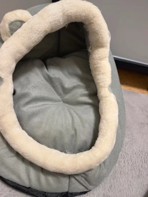 Grå sovsäck för husdjur - Jag har inte använt den, den är ren. Säljer på grund av jag köpte aldrig katt så vill sälja. Jätte fin med grå och vit färg och två små öron.  Mjuk djurbädd i grått och beige material med en rund form och vadderade kanter. Passar små till medelstora husdjur för vila och sömn.