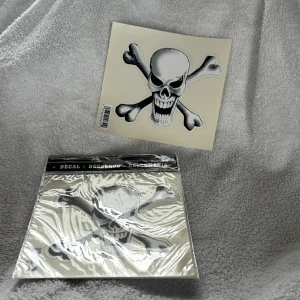 Svartvit dödskalle-dekal XCar - Två stora dekaler med dödskalle och korslagda ben från XCar.  Motiv i svart och vitt med grymt uttryck, perfekt för att sätta på bil, motorcykel eller skateboard.  Klistermärkena har tydliga detaljer i trycket. Helt oanvända. 25kr för båda