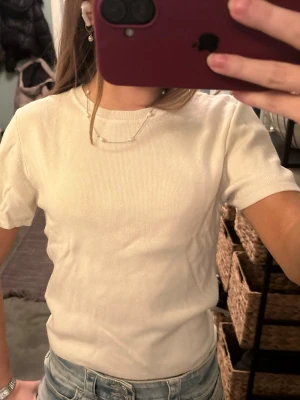 Vit ribbad t-shirt från Gina Tricot - Säljer en enkel och fräsch vit t-shirt från Gina Tricot i storlek M. T-shirten har korta ärmar, rund hals och är ribbad i materialet vilket ger en snygg struktur. Perfekt till jeans eller kjol för en clean look. Lite kräm vit!