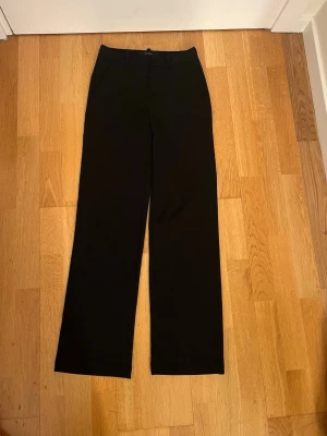 Svarta kostymbyxor från Vero Moda XS - Svarta kostymbyxor från Vero Moda i storlek XS/30. Byxorna har raka ben, normal passform och klassisk design med hällor för bälte och sidfickor. Perfekta för en clean och stilren look.