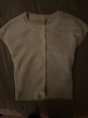 Vit kortärmad kofta från Nelly XS💞 - Säljer en vit, kortärmad kofta från Nelly i storlek XS. Koftan har rund hals, ribbade kanter och knappar framtill. Den är i bra skick💞💞