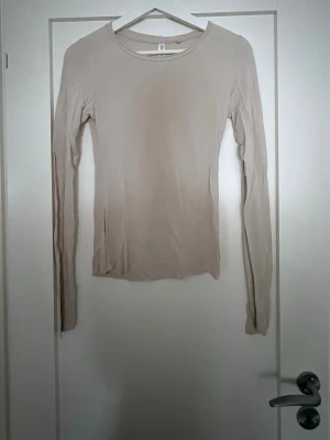 Beige långärmad topp från KappAhl - En enkel och stilren beige långärmad topp från KappAhl. Modellen har rund halsringning och är gjord i ett mjukt och stretchigt material som sitter skönt mot kroppen. Perfekt att matcha med jeans eller kjol för en clean look.