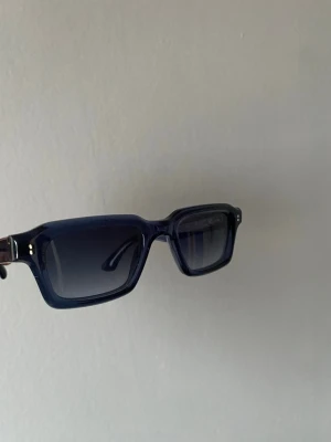  CHIMI SOLGLASÖGON CORE 03 - Säljer ett par stilrena CHIMI Core 03 solglasögon i färgen Indigo. Glasögonen har en rektangulär form med tjock, blå plastbåge och tonade linser. Designade i Stockholm och passar perfekt för dig som gillar en modern och edgy look. Priset kan diskuteras vid snabb affär, original pris 1400kr