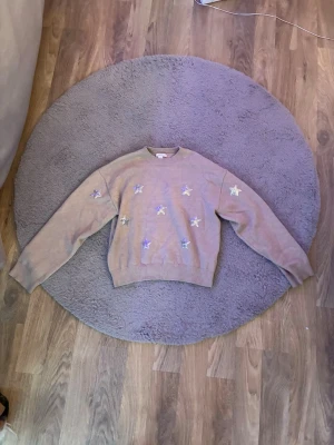 Beige stickad tröja med stjärnor Gina Tricot - Superfin beige stickad tröja från Gina Tricot med glittriga stjärnor på framsidan och ärmarna. Tröjan har rund hals, ribbade muddar och lång ärm. Perfekt för dig som gillar lite extra detaljer och vill ha en mysig look.