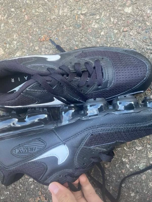 Svarta Nike Air Max sneakers - Säljer ett par svarta Nike Air Max sneakers med cool transparent sula och klassisk snörning. Ovandelen är i mesh och syntet med vita detaljer på sidan. Perfekt för dig som gillar sportig stil och vill ha något som sticker ut med Air Max-dämpning.