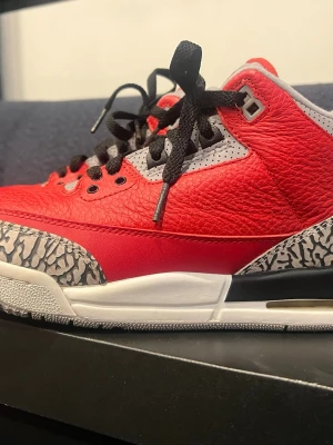 Nike Air Jordan 3 Retro Röd/Grå - Nike Air Jordan 3 Retro sneakers med röd och grå ovandel i skinn och syntet, svart snörning och ikoniskt elephant print-mönster på tå och häl. Sulan är vit med röda detaljer och tydlig Jordan-logga undertill. Perfekt för dig som gillar klassiska och snygga sneakers.